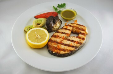 Salmon steak and vegetables baked on a grill served on white plate 
