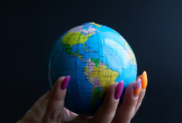 A woman's hand with gel polish shellac manicure holds a small globe with the American continent....