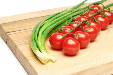 Bunches of fresh red cherry tomatoes and young green onion on cutting board isolated on white background. Ripe tomatoes on green stems. Bunch of fresh onion. Fresh organic vitamin vegetables.
