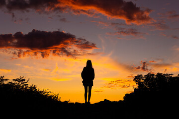 Silhouette of woman with camera standing on hilltop watching sunset
