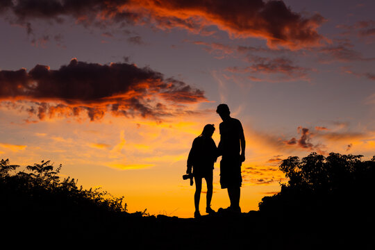 Silhouette of a couple standing on a hilltop beneath a colorful red sunset sky