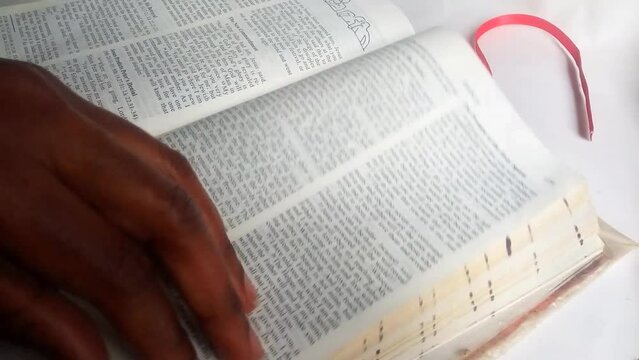 An African lady's hand holding a blue colored pencil, looking and finding a bible verse then marking it by underlining text. Flipping. Placing red ribbon book mark. Christianity concept