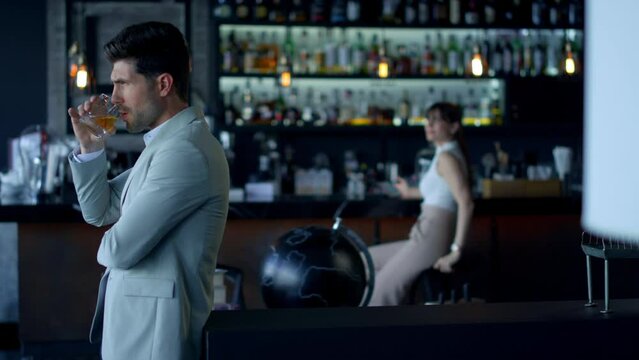 Businessman drinking scotch at restaurant. Woman silhouette sitting at bartender
