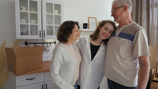 Senior parents give key to new apartment to smiling daughter. Happy young woman hugs elderly mom and dad feeling thankful for gift standing in kitchen