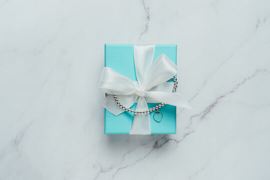 Barcelona, Spain - July 2022.. Tiffany and Co branded gift box with heart bracelet from world-famous American fashion brand. Luxury, trendy jewelry present on marble background