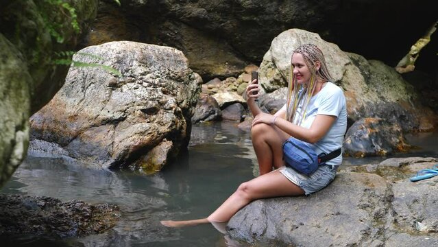Pretty woman takes selfie picture with smartphone. Stream water with stone and rock background