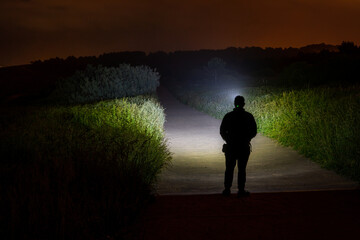 persona con linterna andando por un camino peatonal de noche - obrazy, fototapety, plakaty