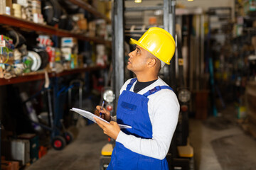 Focused Hispanic salesman checking goods availability on shelves of building materials hypermarket