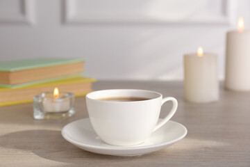 Fototapeta na wymiar Cup of aromatic coffee and burning candles on wooden table indoors