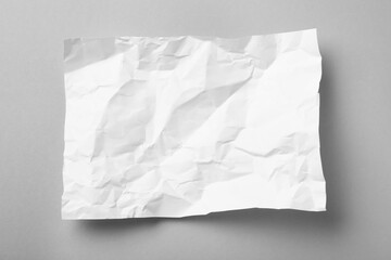 Sheet of white crumpled paper on grey background, top view