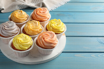 Stand with tasty cupcakes on light blue wooden table, space for text