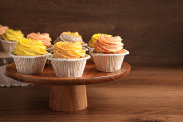 Stand with tasty cupcakes on wooden table. Space for text