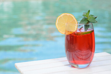 Glass of delicious cocktail on white wooden table near swimming pool, space for text. Refreshing drink