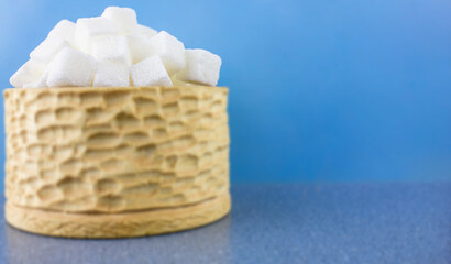 Sugar in a wooden bowl in blur. Sugar in cubes on a blue background in a wooden bowl of blur.