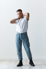 Fototapeta na wymiar Full body shot of handsome serious tanned man guy in basic t-shirt holds hand behind head posing on white background. Fashion Style New Collection Offer. Copy space for ad. Modeling snapshots