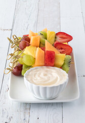 Fresh fruit skewers on a tray served with yogurt dip, ready for eating.