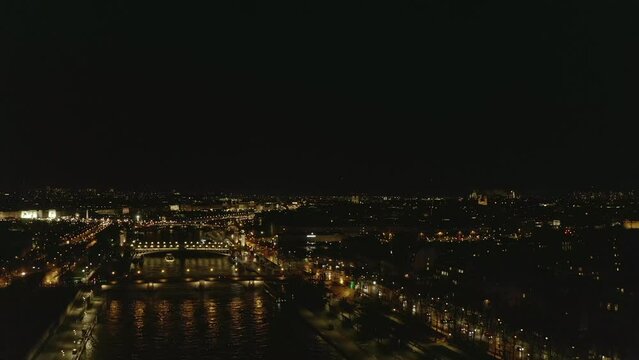 Forwards fly above night city. Illuminated bridges and Seine river waterfronts. Reflection on water surface. Paris, France