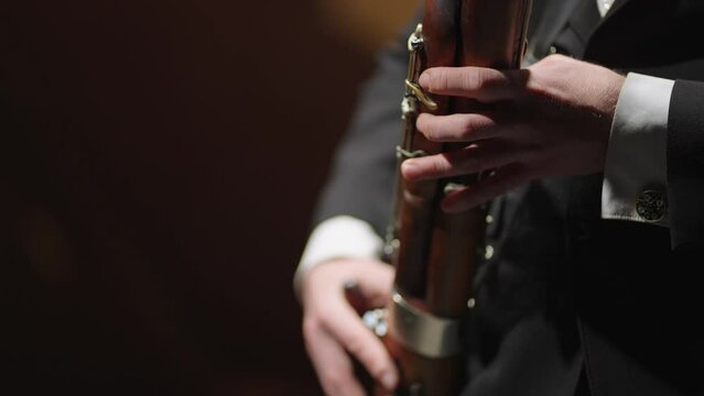 man is playing bassoon in brass orchestra, closeup view of hands of bassoonist, musician is using wind instrument