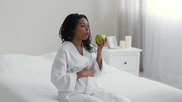 Healthy nutrition during pregnancy. Young happy african american eating fresh green apple, slow motion, free space