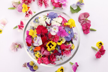 Beautiful colourful yellow violet wite red edible flowers in a small glass bowl on white background...