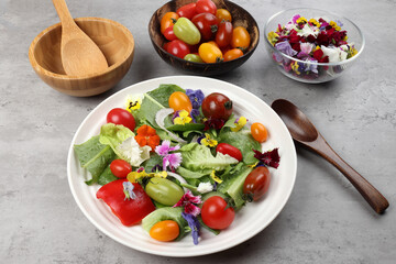 Beautiful colourful yellow violet wite red edible flowers on greed garden salad tomato marble table top bowl wooden spoon on white background copy text space