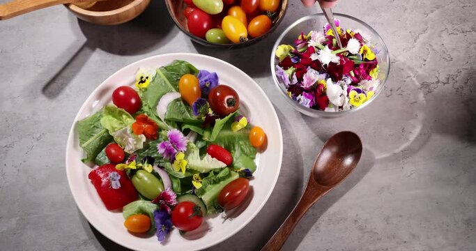 Beautiful colourful yellow violet wite red edible flowers sprinkle spread drop on greed garden salad tomato marble table top bowl wooden spoon on white background