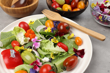 Beautiful colourful yellow violet wite red edible flowers on greed garden salad tomato marble table top bowl wooden spoon on white background copy text space