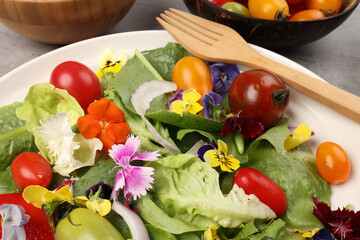 Beautiful colourful yellow violet wite red edible flowers on greed garden salad tomato marble table top bowl wooden spoon on white background copy text space
