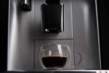 Freshly brewed coffee is poured from the coffee machine into glass cups.