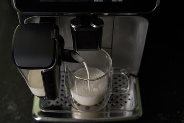 Freshly brewed cappuccino is poured from the coffee machine into glass cups.