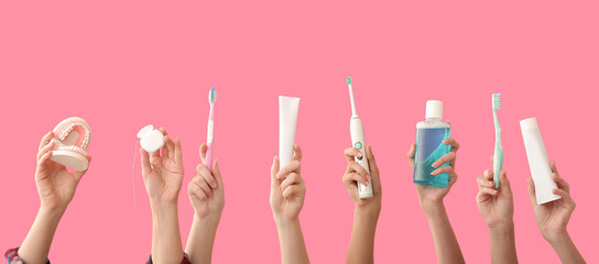 Many hands with toothbrushes, paste, mouth rinse, jaw model and dental floss on pink background