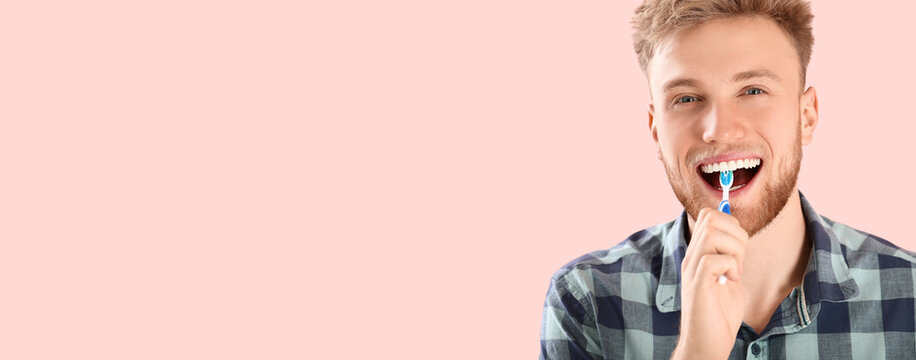 Happy young man brushing teeth on pink background with space for text