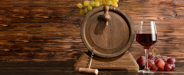 Barrel with glass of red wine and corkscrew on wooden background