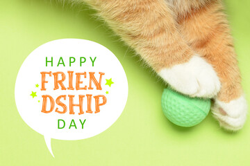 Paws of cute red cat with toy ball on green background. Happy Friendship Day