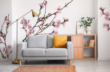 Creative interior of modern living room with grey sofa and printed beautiful blossoming branches on wall