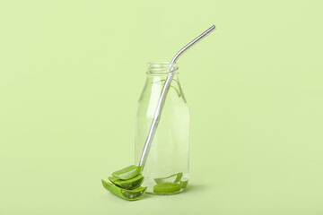 Glass bottle of aloe juice with leaves on green background