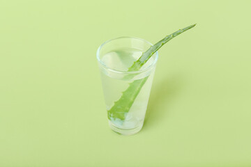 Glass of aloe juice with leaf on green background