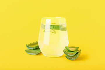 Glass of aloe juice with leaves on yellow background