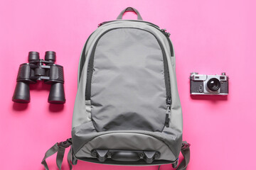 Traveler backpack, binoculars and photo camera on color background
