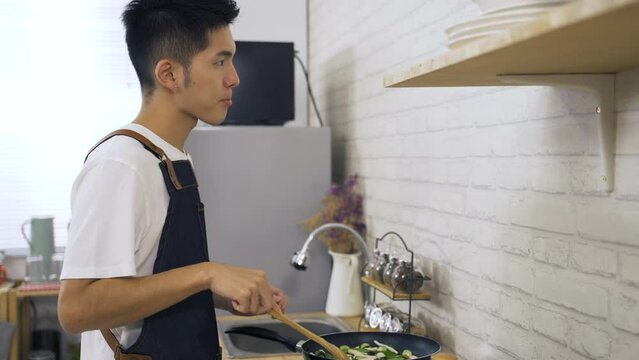 side portrait asian young husband cooking lunching is nodding head while trying his just passage vegetable dish at the kitchen stove in the apartment.