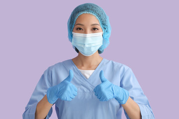 Asian nurse in medical mask showing thumb-up on color background