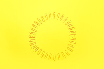 Frame made of yellow paper clips on color background