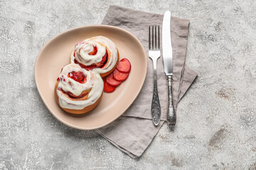 Plate with strawberry cinnamon rolls, cutlery and napkins on grunge background