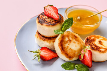 Plate with cottage cheese pancakes, strawberry and honey on pink background, closeup