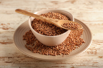Plates and spoon with buckwheat grains on light wooden background