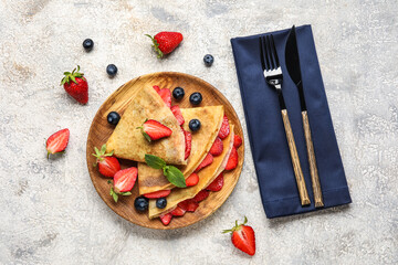 Plate of thin pancakes with berries and cutlery on grunge background