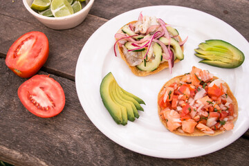 Tostadas de aguachile y ceviche con rebanadas de aguacate, jitomate y limones 