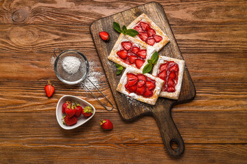 Delicious strawberry puff pastry and sieve with sugar powder on wooden background