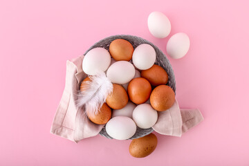 Basket with chicken eggs on pink background