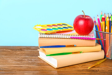 School stationery with apple and paints on table against blue background